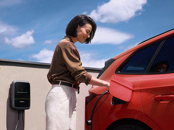 A woman plugging a charger into a red electric vehicle