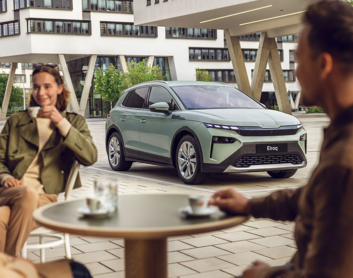 A couple sitting in the foreground, with a mint green Skoda in the focus in the background