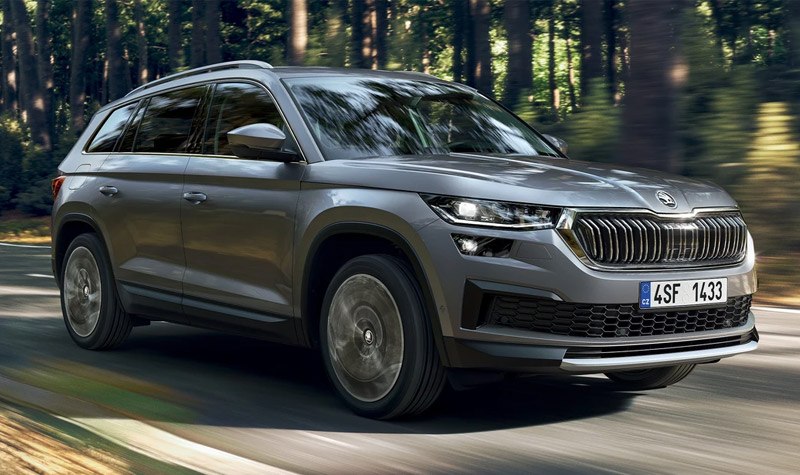 Silver Kodiaq driving down road by a forest