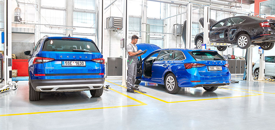 Two blue cars in a bright workshop with a man in overalls inbetween them